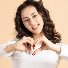 Lifestyle, Valentine's day concept. Beautiful woman showing fingers heart sign and looking at camera with smile. Beige background with copy space. Hands in camera focus