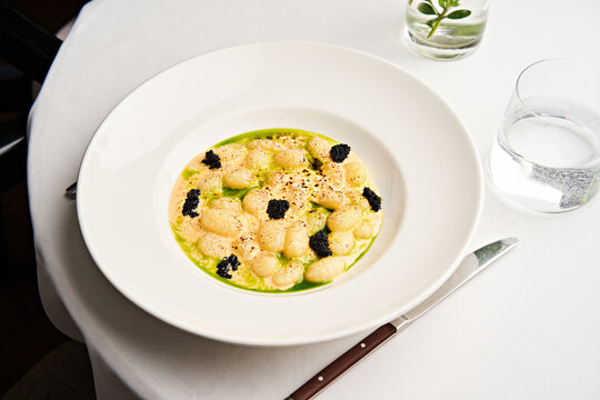 A beautifully plated dish featuring soft gnocchi drizzled with vibrant green sauce and garnished with caviar. This gourmet meal is served in an upscale dining environment