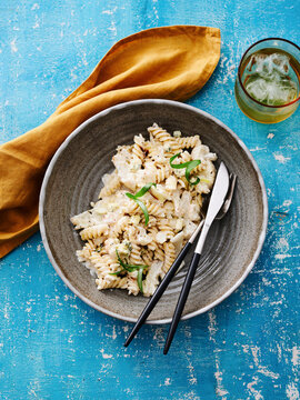 Creamy fusilli pasta. A rustic bowl holds a flavorful pasta mixed with fresh herbs and ingredients. Beside it, a refreshing drink awaits, all set against a bright blue table backdrop