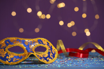 Beautiful carnival mask, ribbons and confetti on color background, closeup