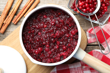 Tasty cranberry sauce in saucepan, berries and cinnamon sticks on wooden table, flat lay