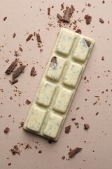 Tasty chocolate bar and crumbs on beige background, top view