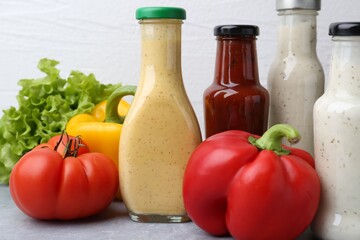 Tasty sauces in glass bottles and fresh products on light grey table, closeup