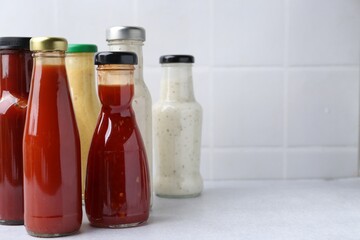 Tasty sauces in glass bottles on white table, closeup. Space for text