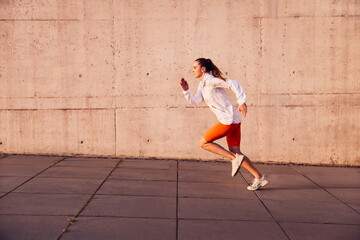 Fit woman running outdoors against concrete wall