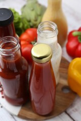 Tasty sauces in glass bottles and fresh products on white wooden table, closeup