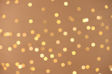 Blurred view of golden lights on light background, bokeh effect