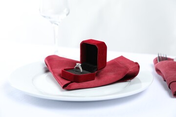 Beautiful engagement ring and setting for romantic dinner on white background, closeup