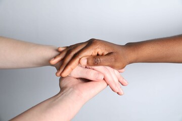 Stop racism. People of different skin colors holding hands on light grey background, closeup