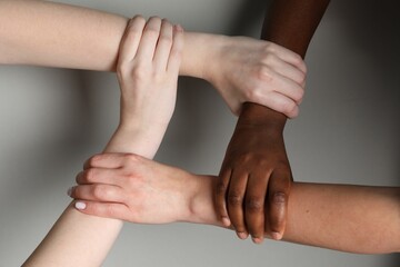Stop racism. People of different skin colors joining hands on light grey background, closeup