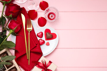 Romantic place setting for Valentine's day. Cutlery, napkin, plate, roses and decorative hearts on pink wooden table, flat lay. Space for text