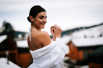 Woman in white swimsuit relaxes in hot water amidst winter mountains and snow-covered landscape