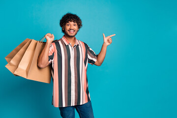 Portrait of nice young man bags direct finger empty space wear shirt isolated on turquoise color...