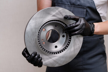 Auto mechanic holds new brake disc in hands, close-up. Auto parts replacement concept, car...