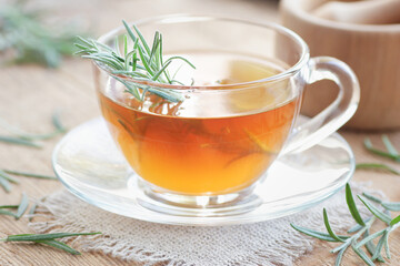 Rosemary herbal tea in a glass cup with fresh leaves on wooden rustic background, closeup, immune, skin and hair healing drink, natural medicine and naturopathy concept
