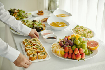 Close-up of waiter setting delicious snacks and plates with fruits on dining table
