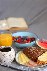 Tray with various healthy breakfast food, open book and reading glasses on the bed. Breakfast in bed concept. Selective focus.