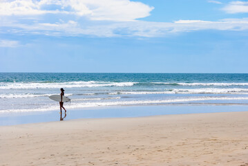 Young woman surfer walking along the beach with a surfboard on a sunny day