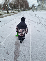 Child discovering first snow. A little boy cleans a path from the snow with a toy shovel. Toddler with a snow shovel photoshooted from the back.