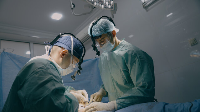 Surgeon doctor with intern practitioner perform surgical operation men cut out appendicitis cancer tumor operate heart lungs stomach incision sew up wound surgery process in clinic hospital healthcare