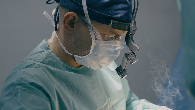 Close up doctor man physician practitioner surgeon medic in protective medical mask perform surgical operation microscope plastic surgery cautery modern medical treatment medicine hospital health care