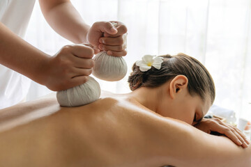 Hot herbal ball spa massage body treatment, masseur gently compresses herb bag on woman body....