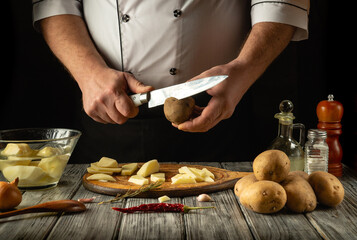 A skilled chef expertly peels and chops fresh potatoes in a rustic kitchen setting. The wooden table is adorned with various kitchen tools and ingredients, creating a warm and inviting atmosphere