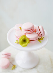 Decoratively arranged pink macarons on a white pedestal stand with green floral accent in a bright setting