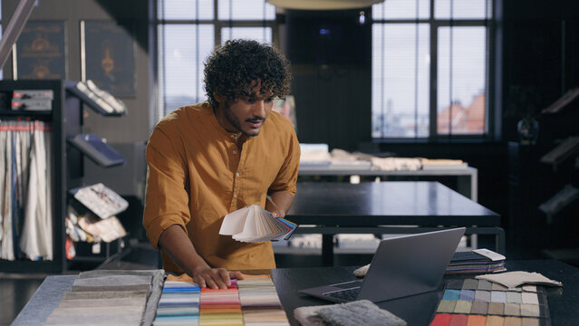 Indian Arabian man creative fashion designer stylist decorator salesman businessman talking video call using laptop show fabrics clothes new material samples offer to client online meeting in atelier - Powered by Adobe