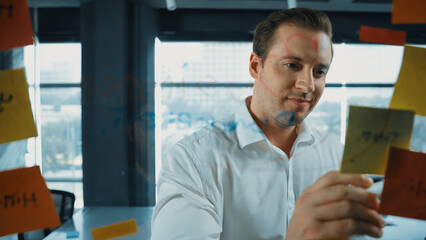 Portrait of professional male leader writing marketing idea on sticky notes. Caucasian businessman...