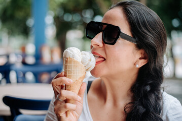 A happy woman eating ice cream while wearing sunglasses.