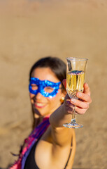 Young woman in festive outfit with mask holding glass of champagne during outdoor birthday or new year celebration.