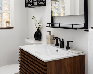 A bathroom sink detail with a mid-century wood cabinet, black faucet on a white sink, and cozy decor.