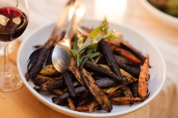 white ceramic bowl of roasted heirloom carrots being served with silver tongs at farm to table restaurant