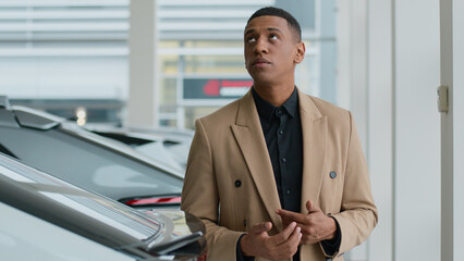 Thoughtful pensive guy male businessman African American man client buyer think choose new automobile in auto salon store thinking puzzled customer think ponder dream buy rent car decision loan credit