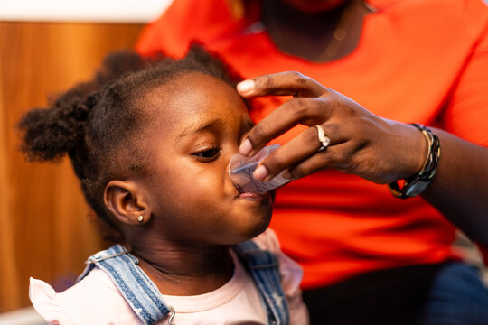 Loving African mother giving her child syrup medicine at home.
