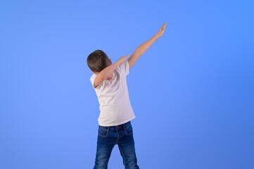 Portrait of elementary boy with arms raised dabbing while dancing against isolated blue background