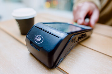 Contactless payment system with nfc technology on pos terminal being used by customer for purchase in cafe