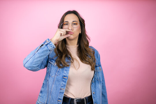 Young beautiful woman wearing denim jacket over isolated pink background mouth and lips shut as zip with fingers. Secret and silent, taboo talking