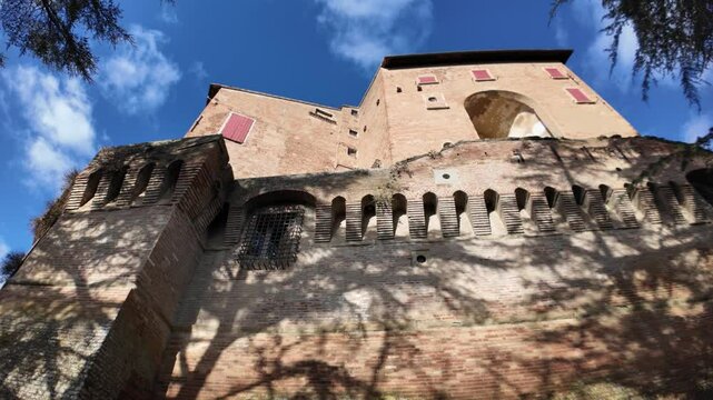 Imposing Dozza Castle rises against a vibrant blue sky, its brick walls and red shutters contrasting beautifully with the picturesque Emilia Romagna landscape