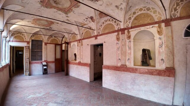 Wide angle view of an interior corridor within Dozza castle, Italy, highlighting decorative frescoes on the ceiling and walls, with sculptures displayed in alcoves, showcasing art and architecture
