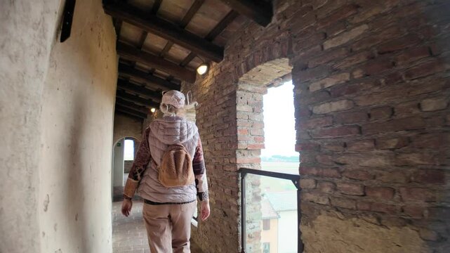 Female tourist admiring the landscape from a circular room inside the medieval fortress of Dozza, Emilia Romagna, with brick walls, wooden ceiling and large windows