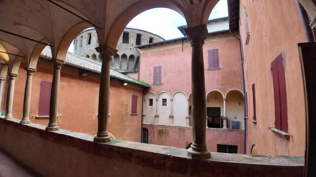 Internal courtyard of Dozza castle with arches, columns, plants and red windows, creating a picturesque and historic atmosphere in Emilia Romagna, Italy