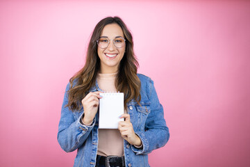 Young beautiful woman wearing denim jacket over isolated pink background smiling and showing blank...
