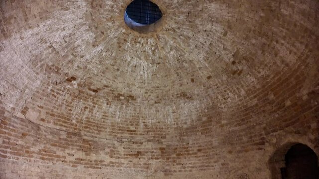 Intriguing view from above into a deep, circular well within Dozza Castle, Italy, revealing weathered walls and debris at the bottom, hinting at a rich, mysterious history