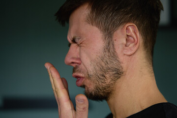 Fototapeta premium Bad breath from mouth. Close-up of man checking his breath by exhaling into his hand, showing concern about oral hygiene or bad breath
