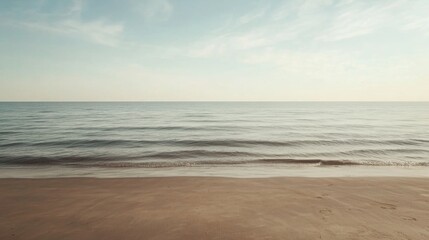 Serene beach landscape with calm ocean and sandy shore under a pale sky.