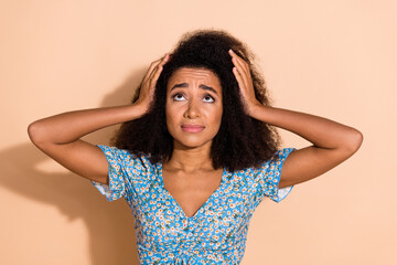 Photo of adorable unhappy girl wear blue top arms head looking up empty space isolated beige color...