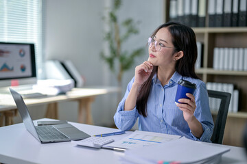 A woman is sitting at a desk with a laptop and a cup of coffee