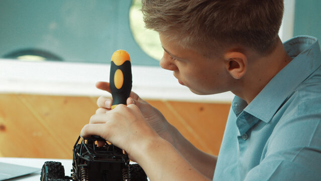 Close up of young student tighten the nut by using screwdriver. Caucasian teenager repairing or fixing car model while inspect robotic machine construction at STEM technology class. Edification.